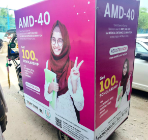 Advertisement for AMD-40 scholarship program displayed on a moving vehicle, featuring a young hijabi student promoting 100% scholarship opportunities.