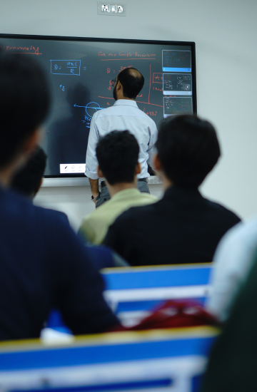 Instructor teaching physics on a digital smartboard at Talent Zone Academy, with students attentively listening in a classroom.